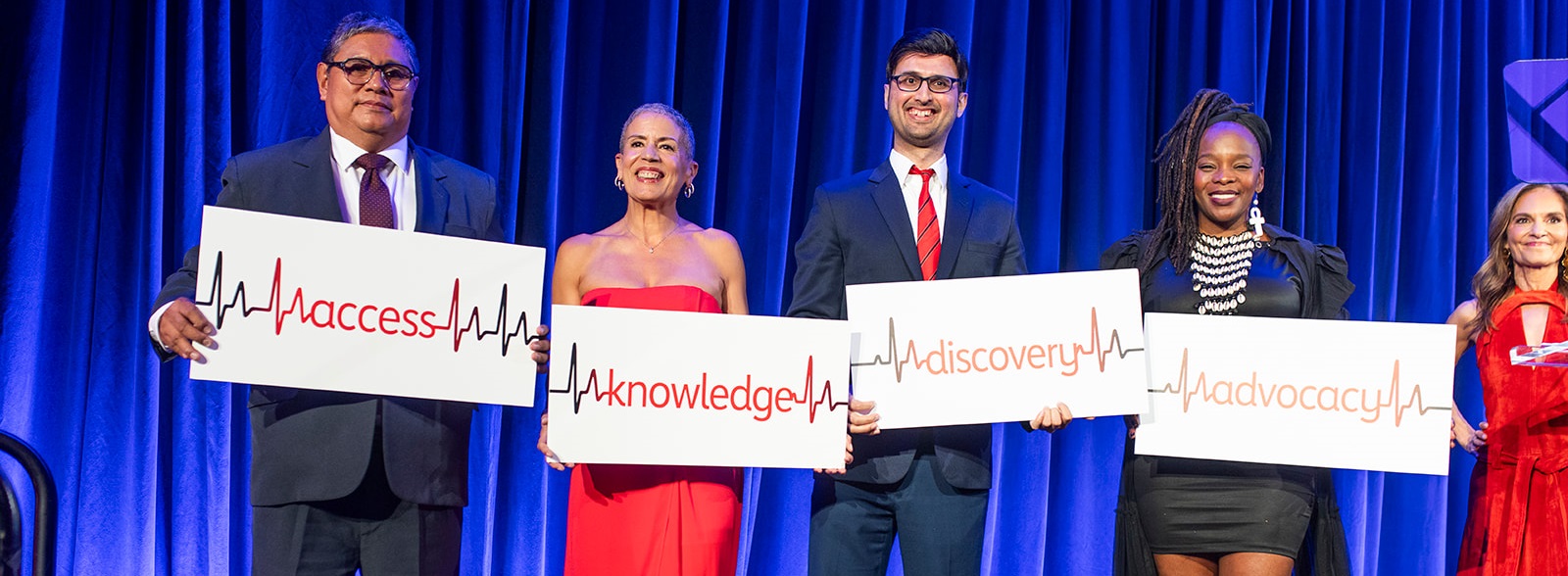 Five people standing on stage holding signs reading access, knowledge, discovery, and advocacy.